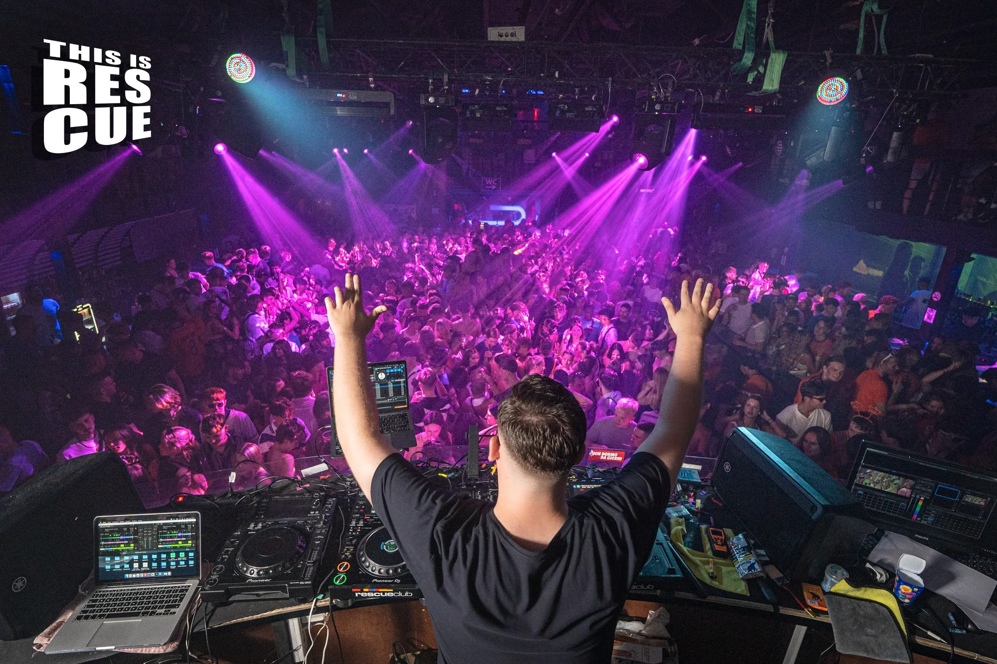 Vextra performing behind the decks to a packed club crowd with both hands raised