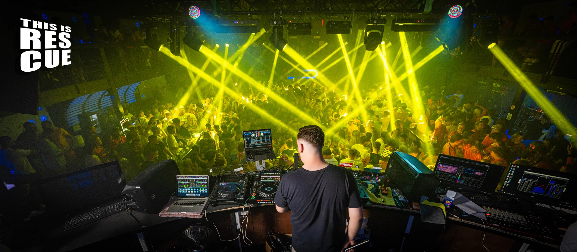 Vextra performing behind the decks to a packed club floor under yellow lighting